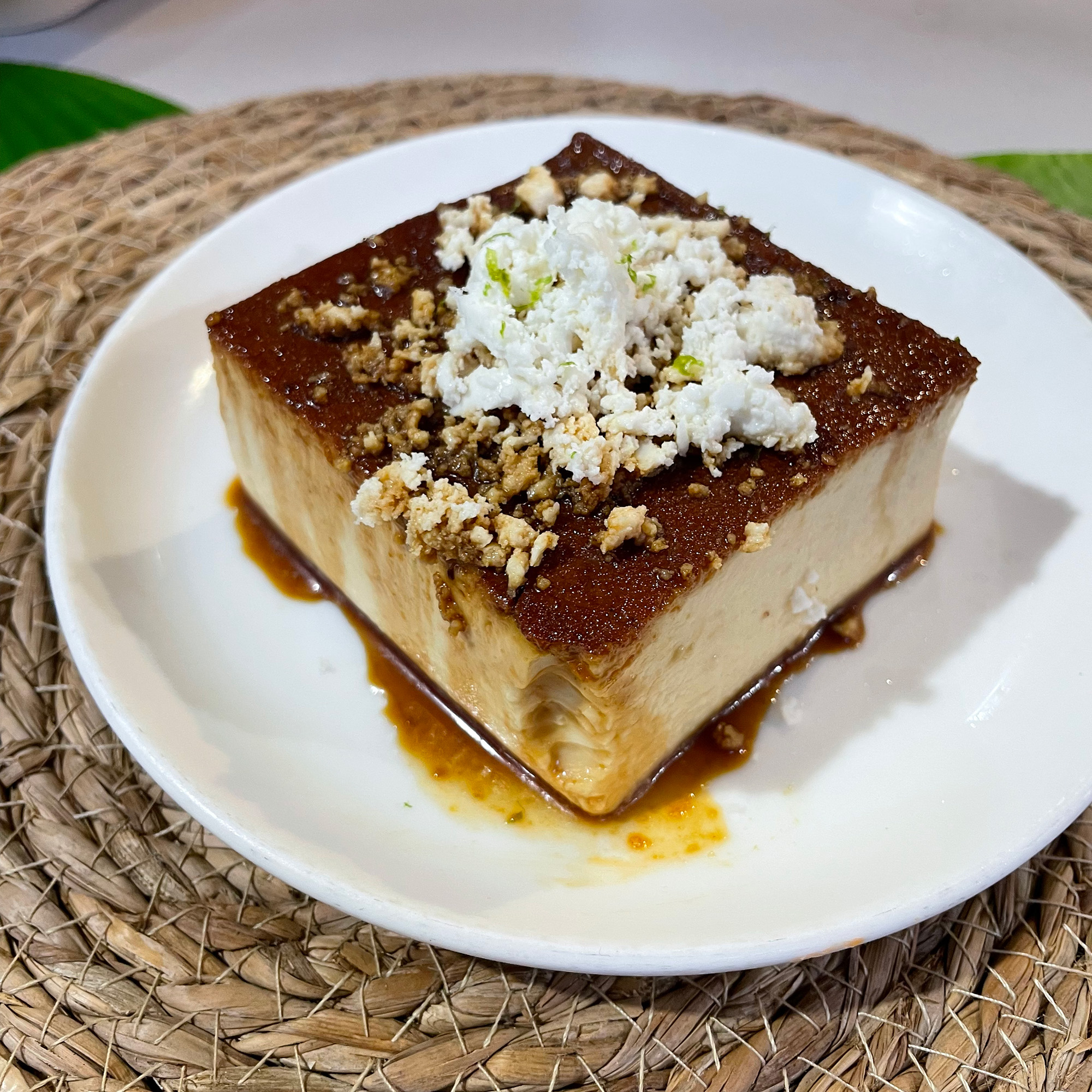 Square of flan drizzled with caramel and topped with crumbled cheese.
