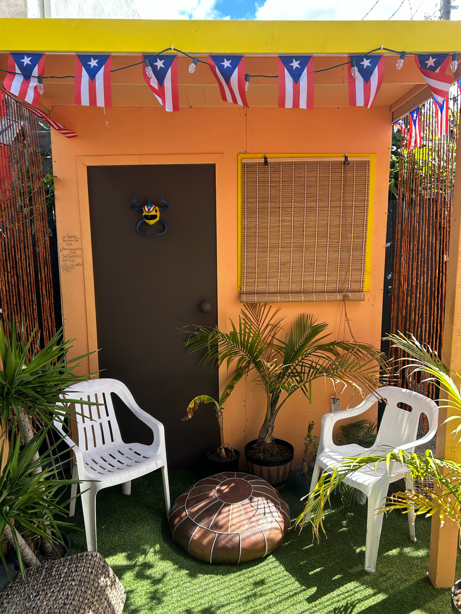 Facade of a yellow traditional Puerto Rican style house, with two plastic patio chairs in front.