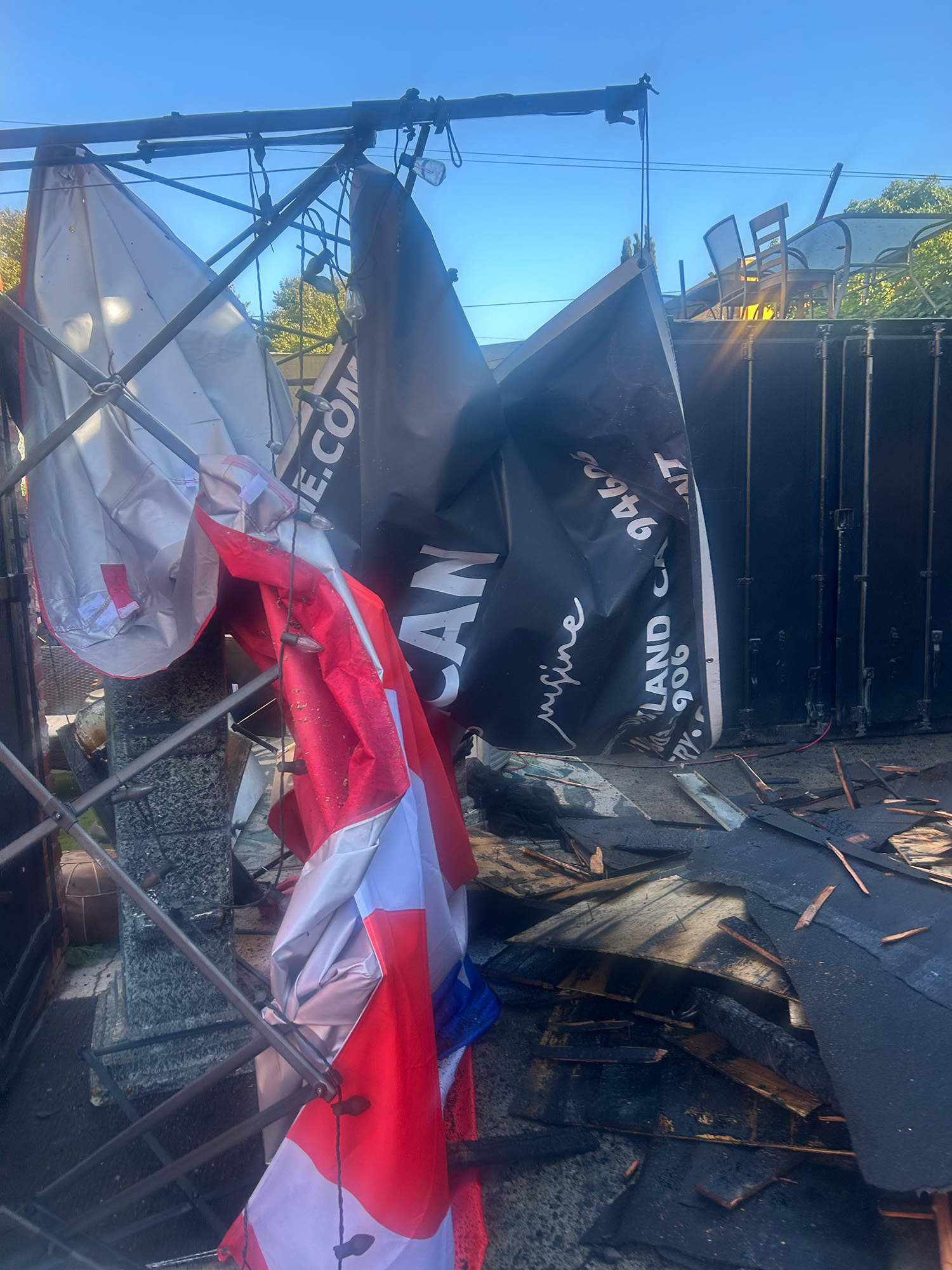 Remains of a restaurant's back patio after a fire, with a banner and a Puerto Rican flag fallen to the ground.