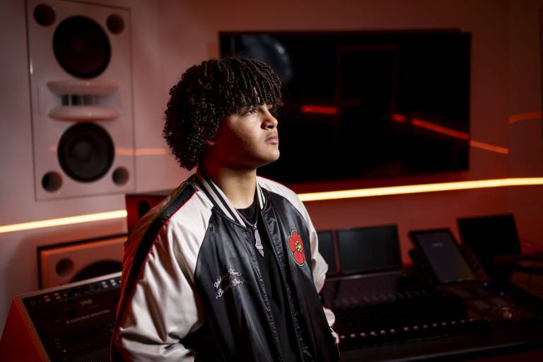A teenage boy with curly hair looks into the distance at a music studio.