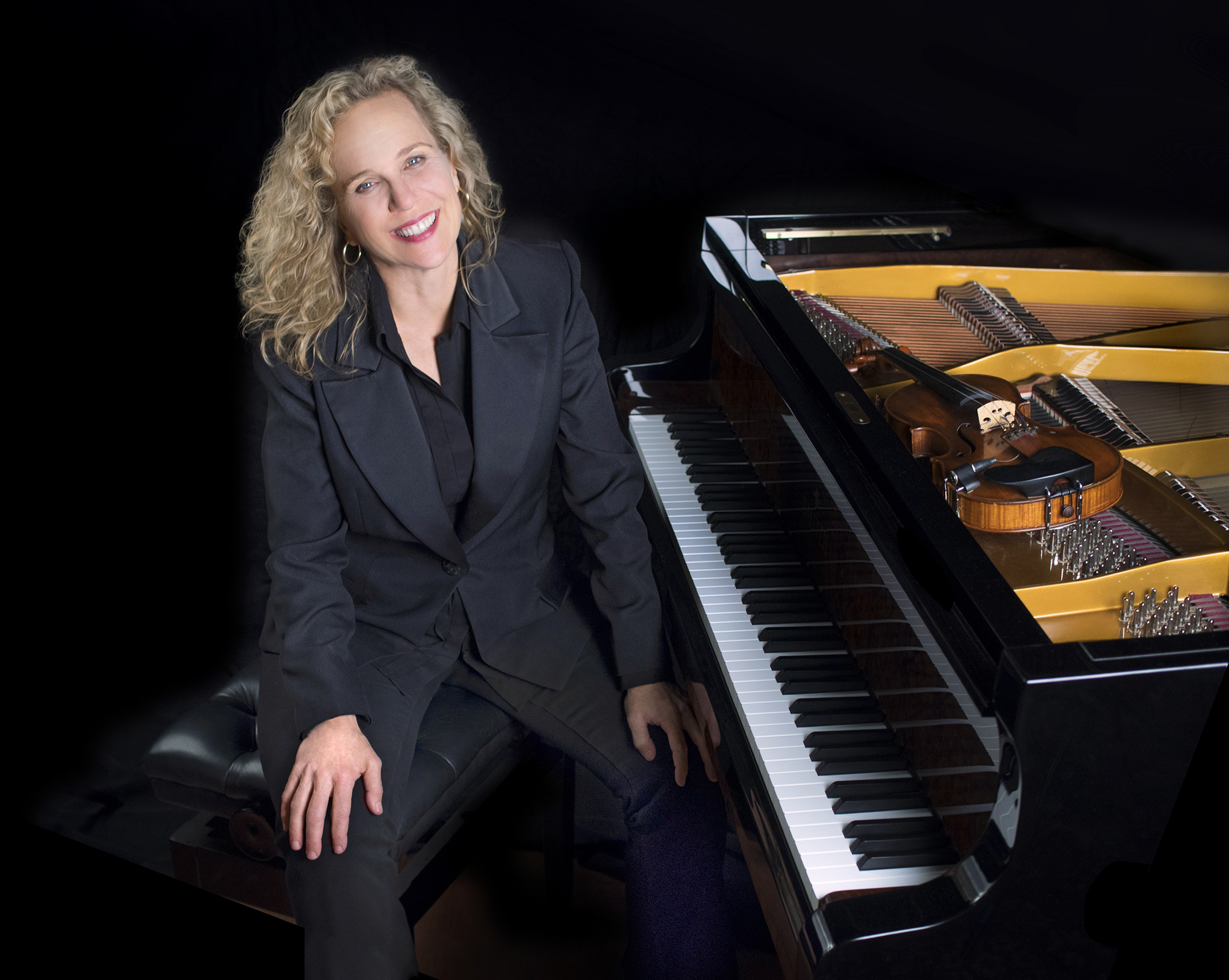 A smiling woman in a dark suit sits at a piano