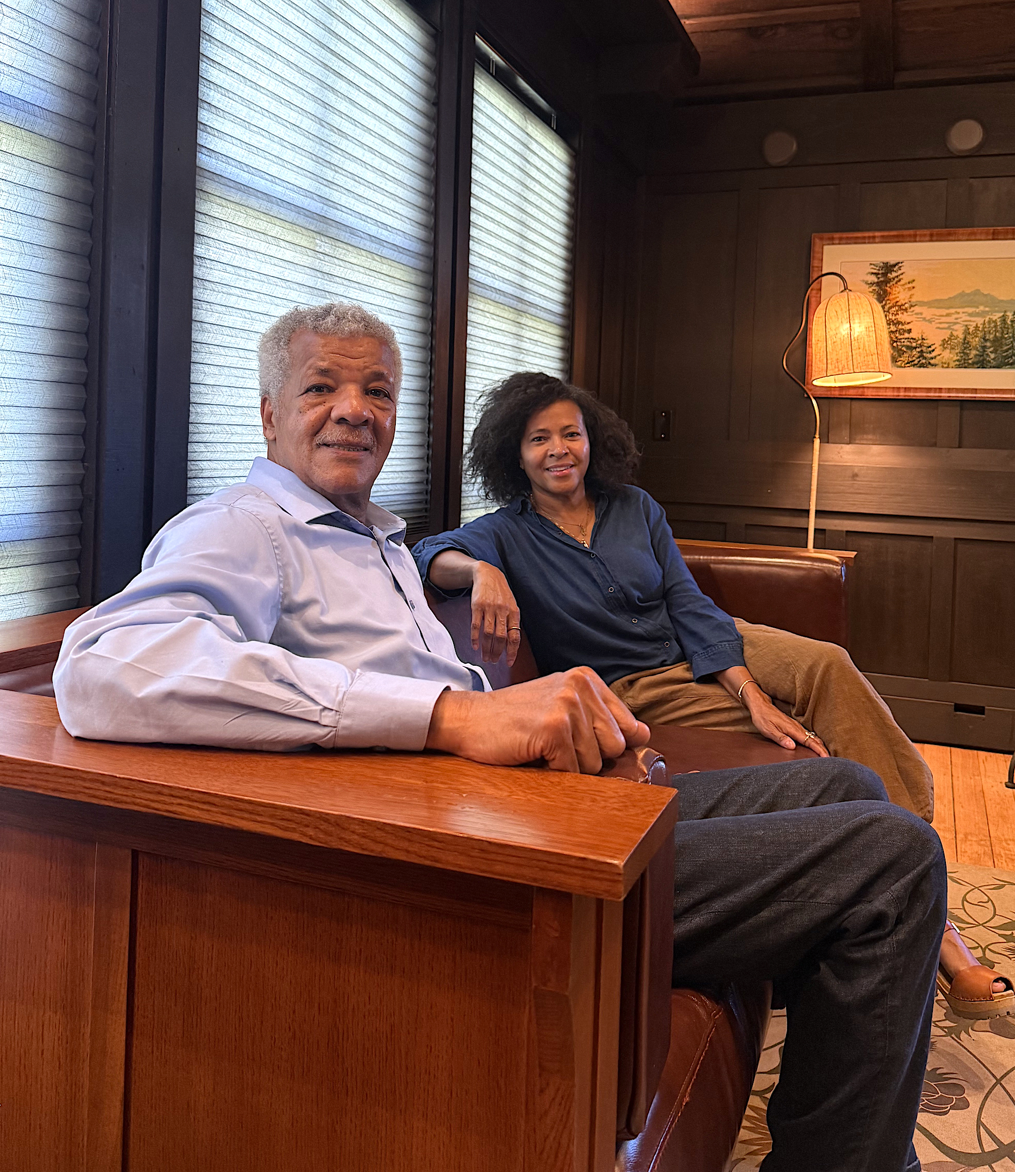 Two people, an older African American man and a middle aged African American woman, sit on a couch and pose for a photo.