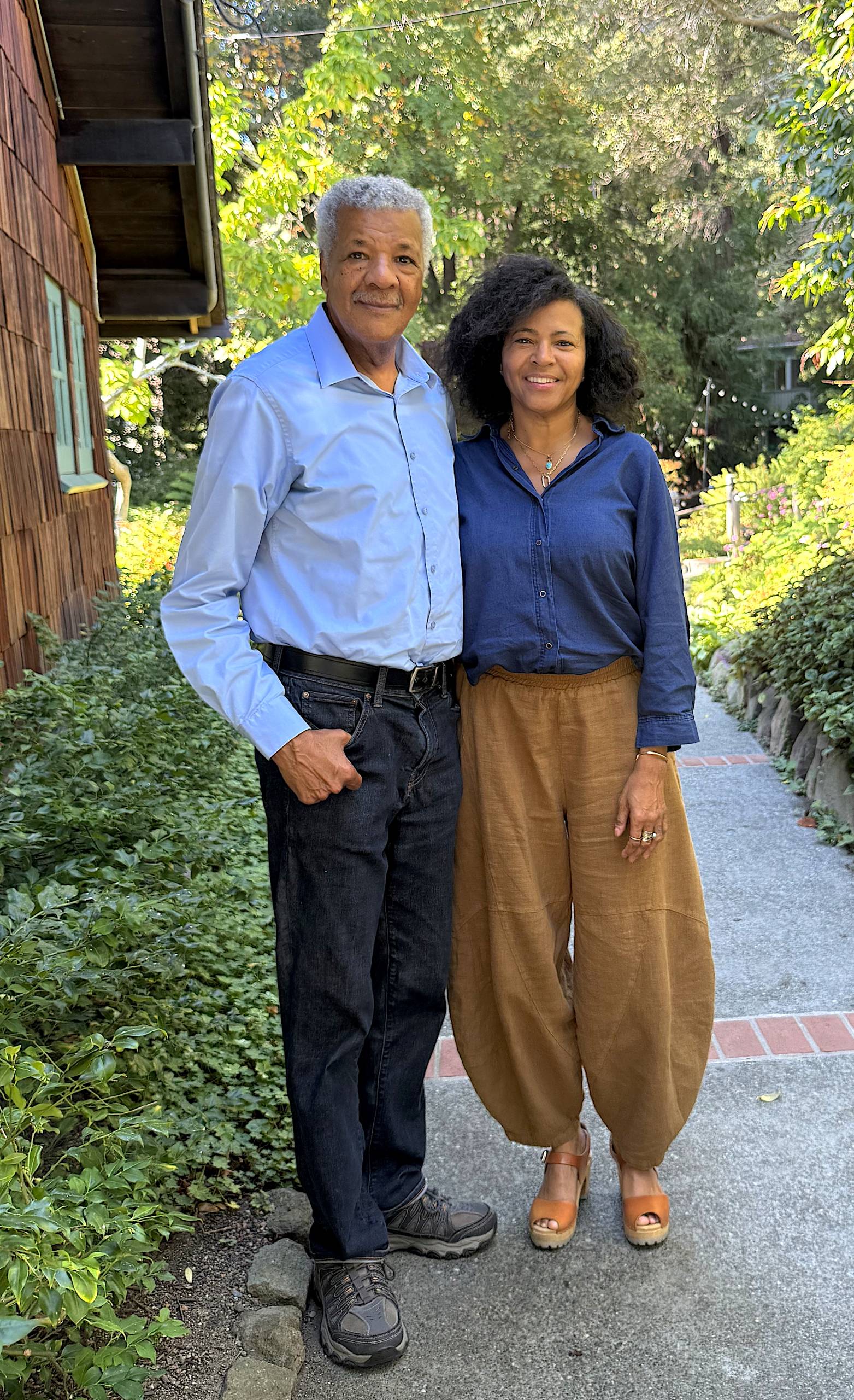 An African-American man and woman pose for a photo outside, on a walkway in a tree-lined area.