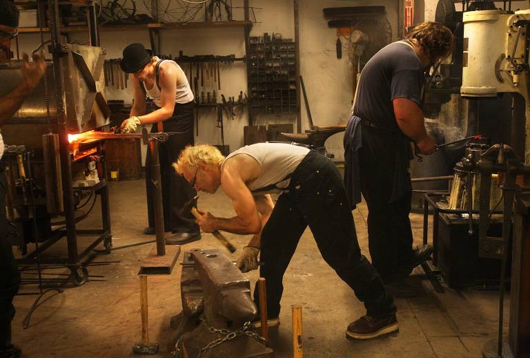 three en work on metal projects with hammers and anvils
