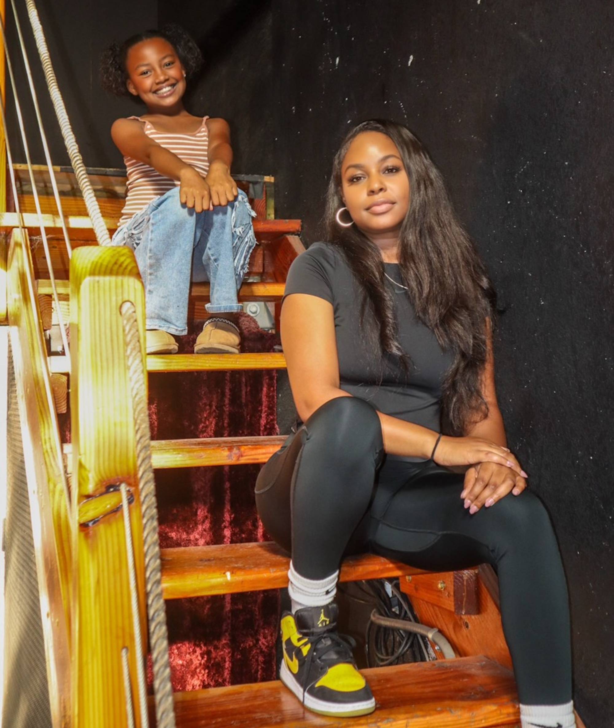 An African-American woman and a young girl pose for photo while sitting on wooden stairs.
