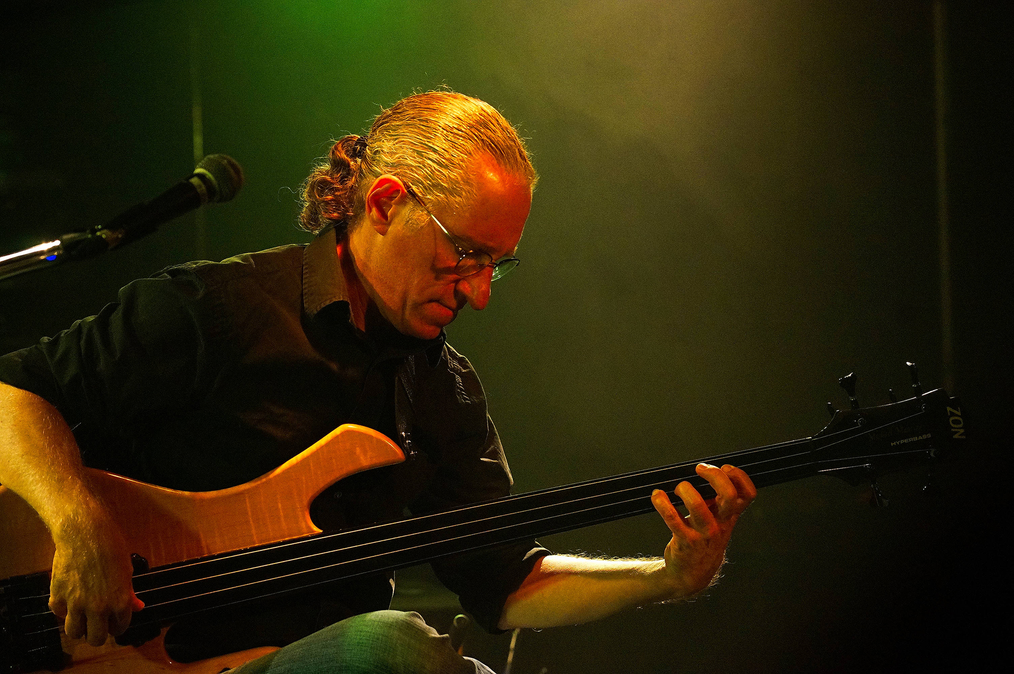 A man in a pony tail and black shirt plays a fretless electric bass guitar