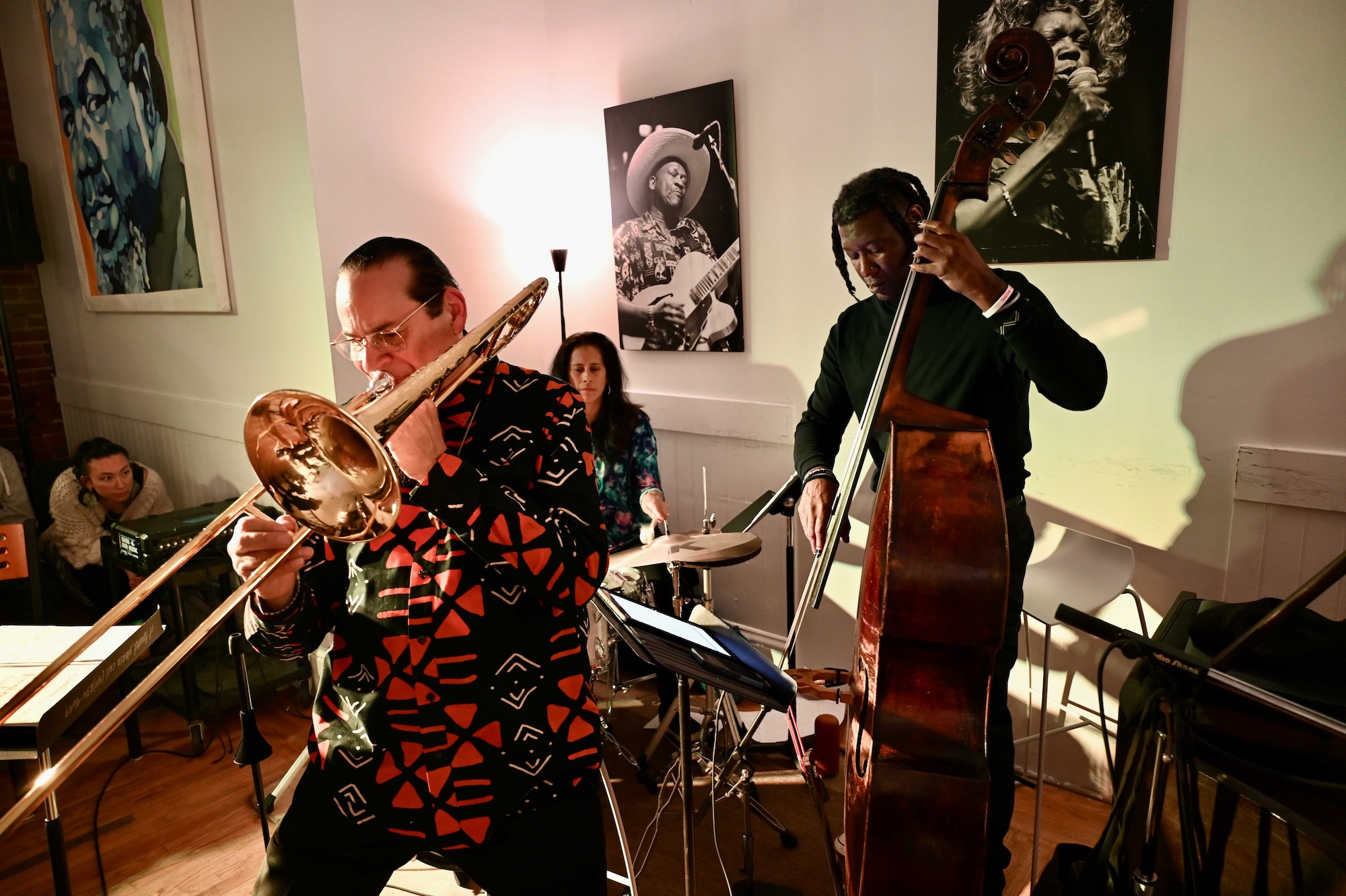 A jazz combo performs against a wall with portraits hanging on it