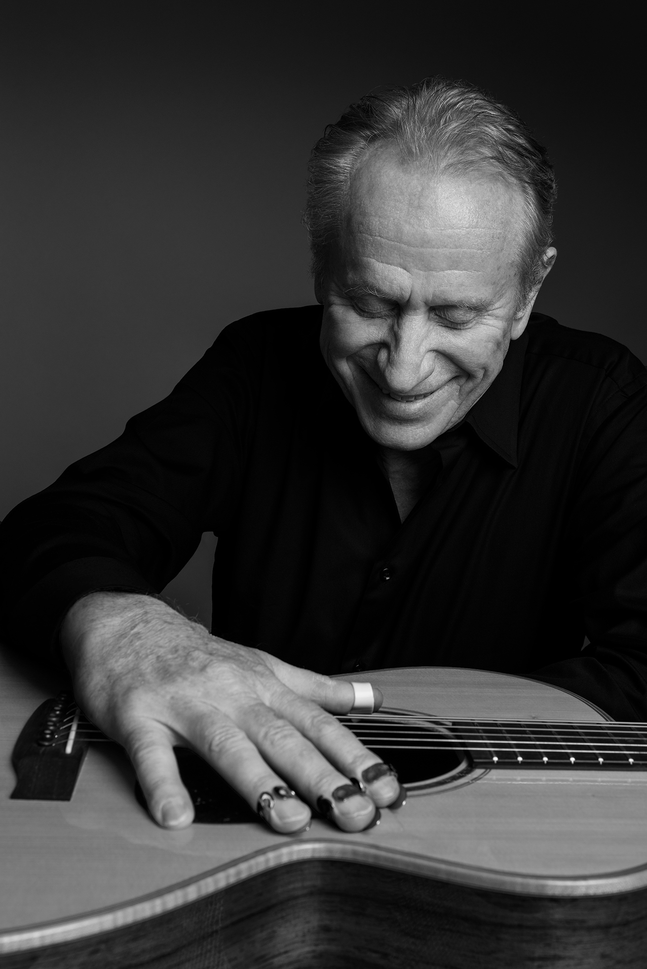 A man in a black shirt gazes downward to an acoustic guitar