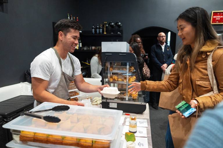Asian man in a chef's apron hands baked goods to a customer.
