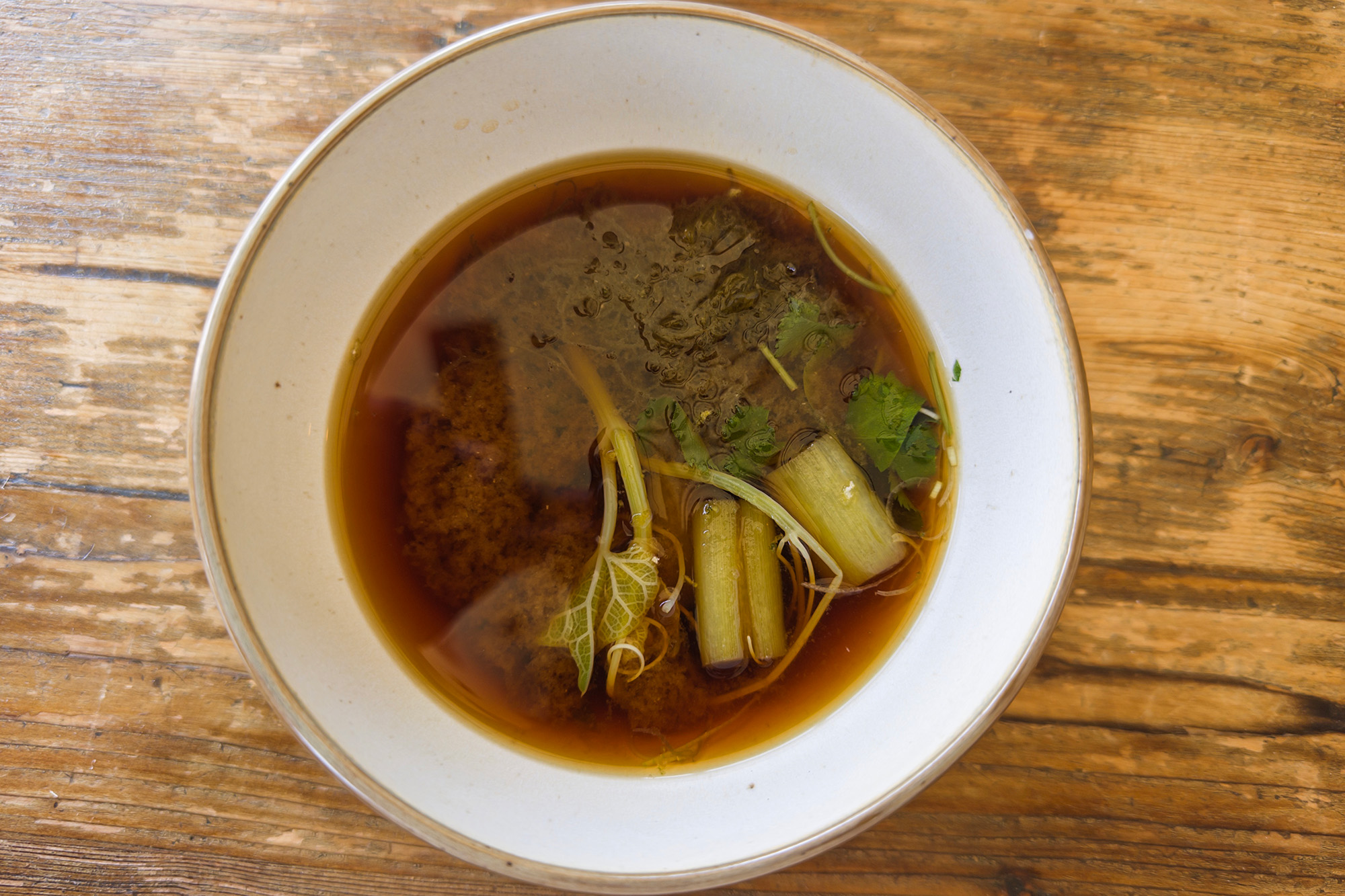 A bowl of dark miso soup loaded with assorted green vegetables.