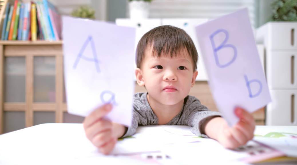 Asian or Asian American kindergarten boy holding up one flash card with a capital 'A' and lowercase 'a' and a second flash card with a capital 'B' and a lowercase 'b'