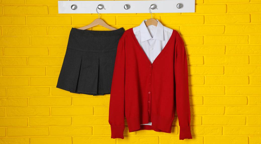 Shirt, jumper and skirt hanging on yellow brick wall. School uniform