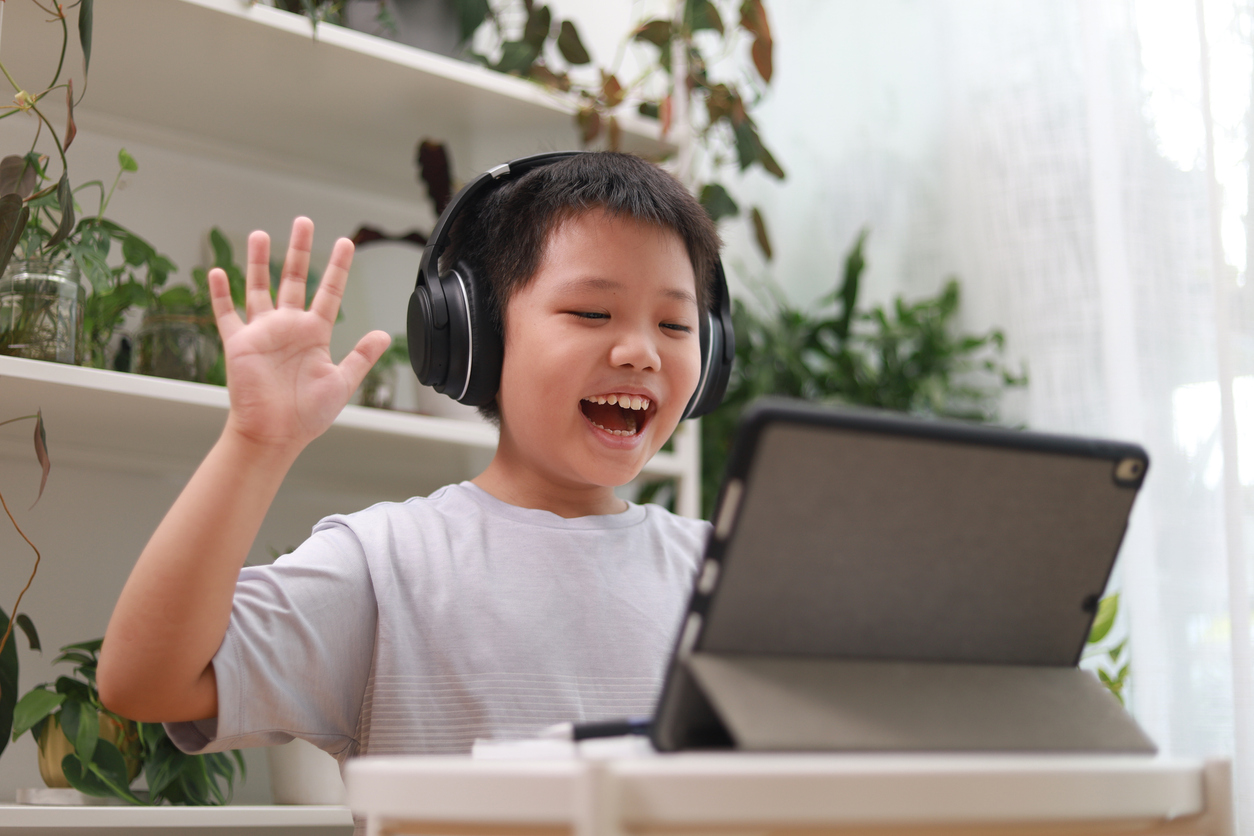 Close up of a young Asian boy studying and doing homework using his tablet computer and headphones.