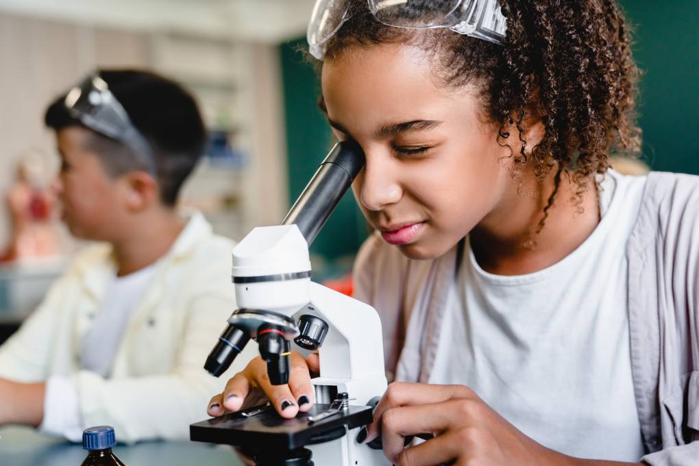 African-american student using microscope at science lesson class at school lab.