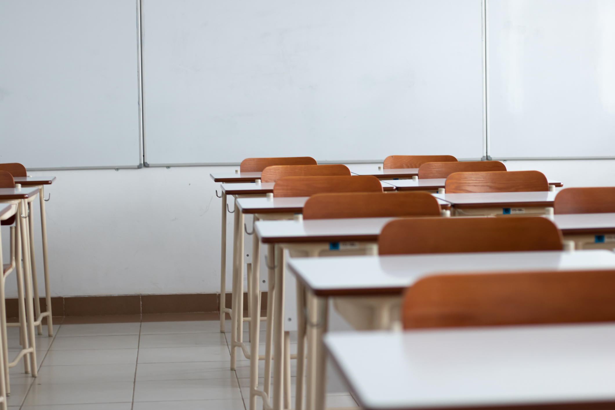 a row of empty student tables and chairs with a white board in the background