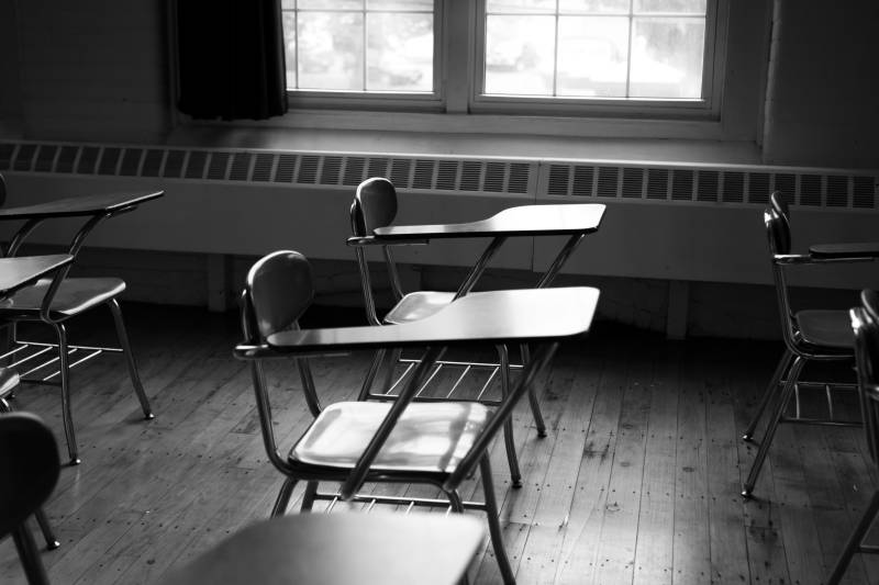 3 empty student desks with attached chairs in a dimly lit classroom. Partial window in the background