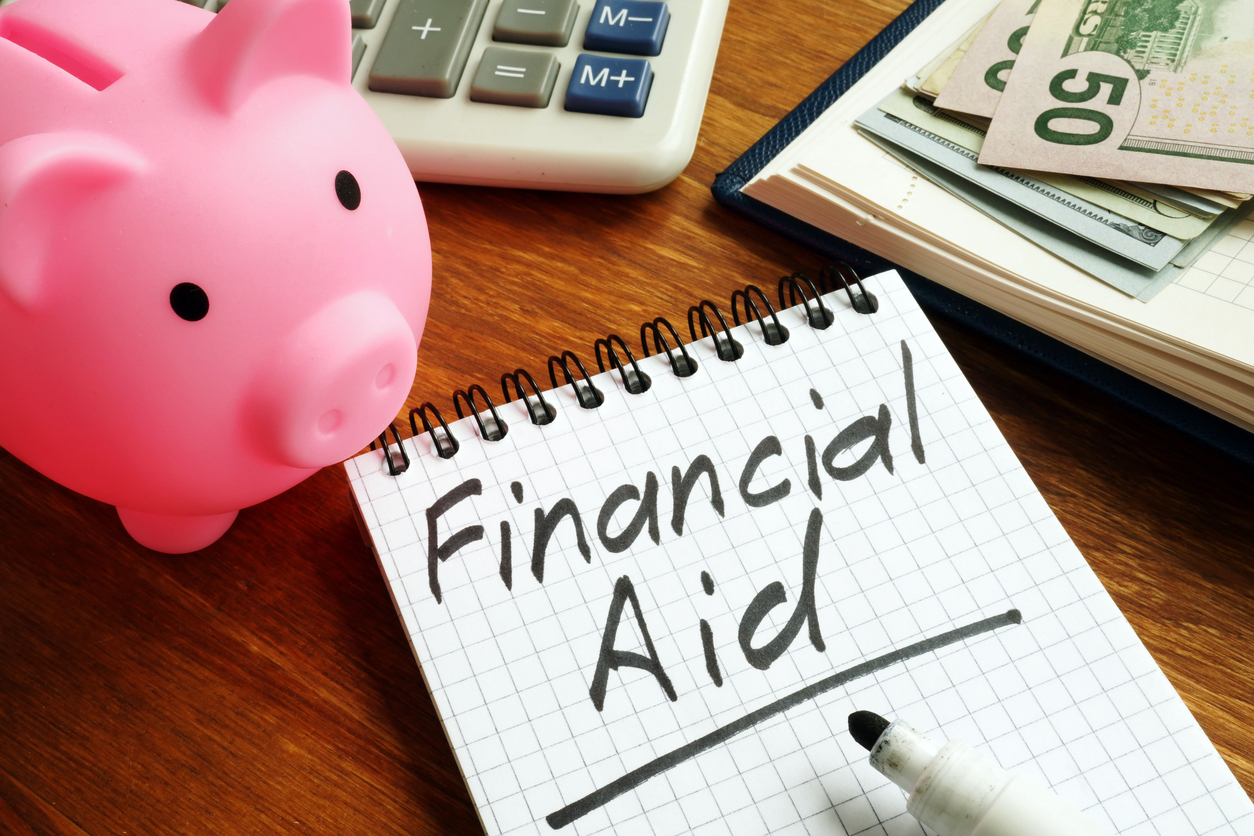 narrow spiral notebook with the words "financial aid." In the corners, dollar bills, a piggy bank and calculator partially enter the frame