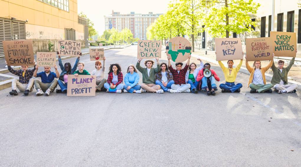 A group of young people protest sit in a road holding cardboard signs about fighting climate change