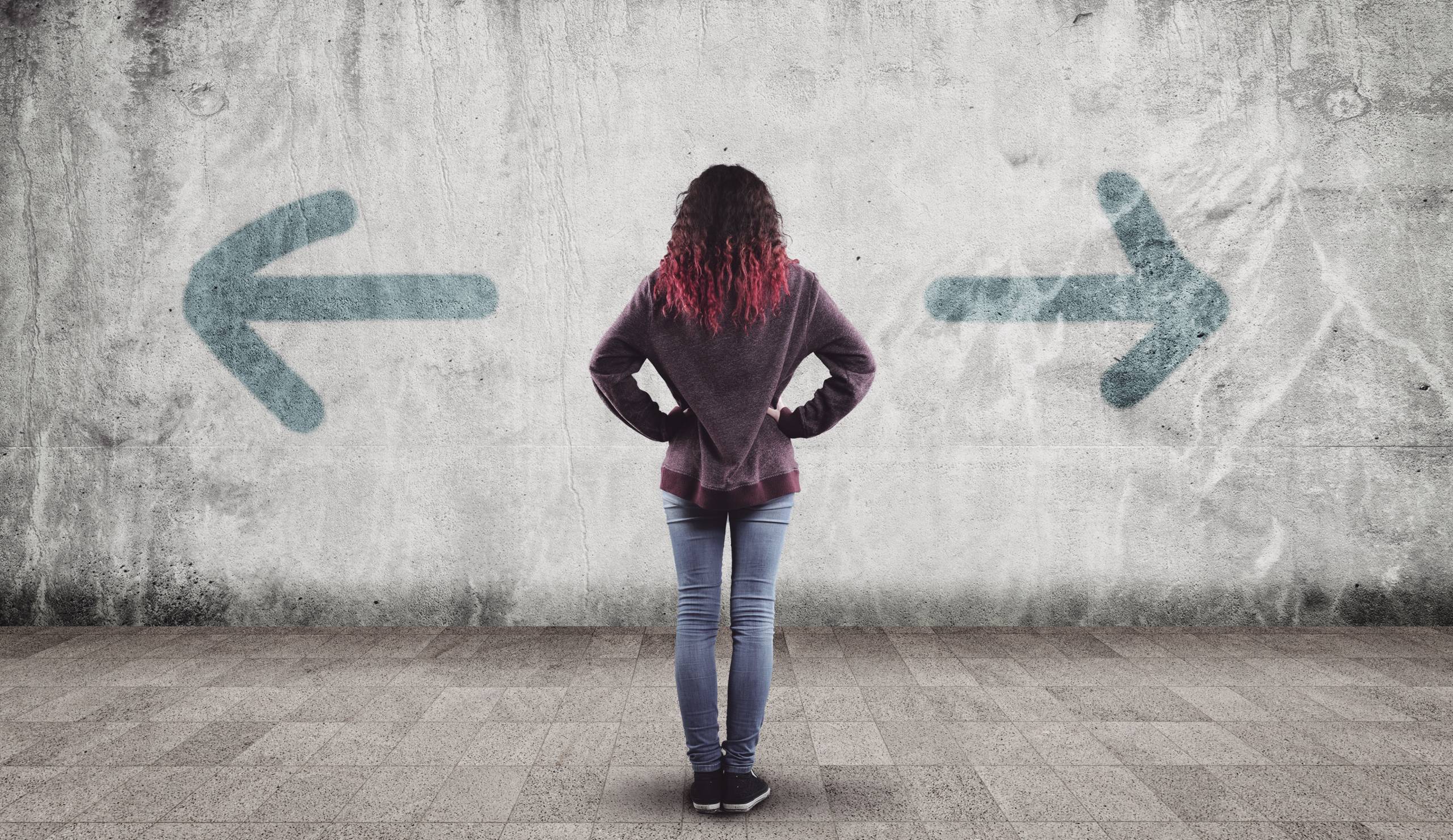 Young girl in front of a wall painted with arrows towards opposite directions.