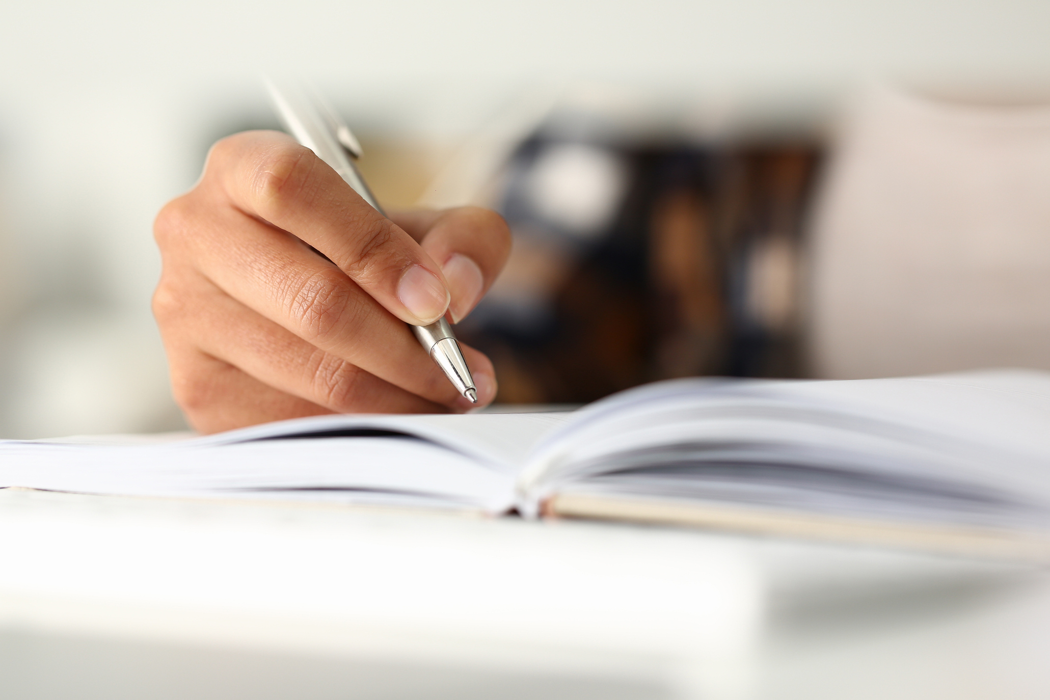 Close up of a hand writing in a journal or notebook with a silver pen