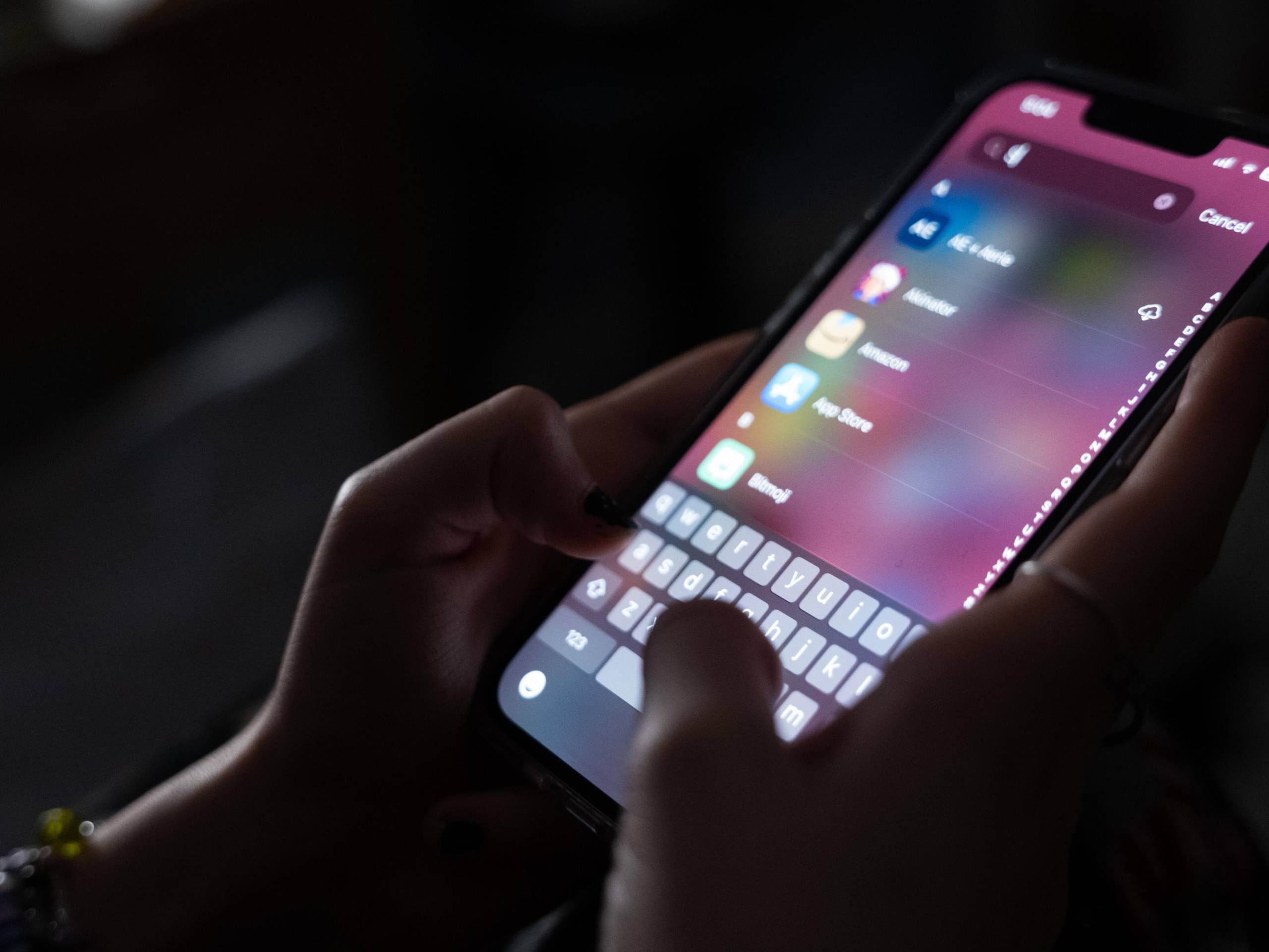 Two hands hold a smart phone. Thumb types in the search field for an app