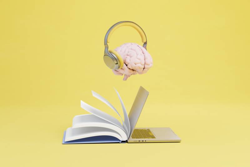 Brain with headphones floating above a book and laptop on a yellow background