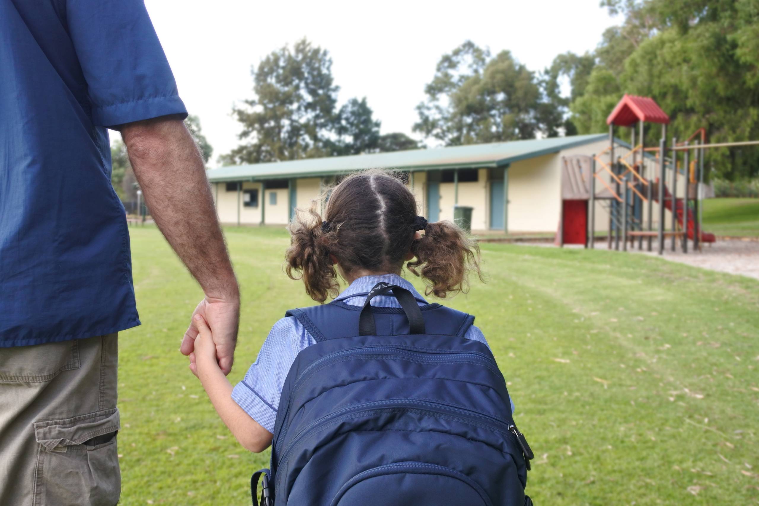 Rear view of schoolgirl holding her fathers hand on the way to school. Real people. Copy space