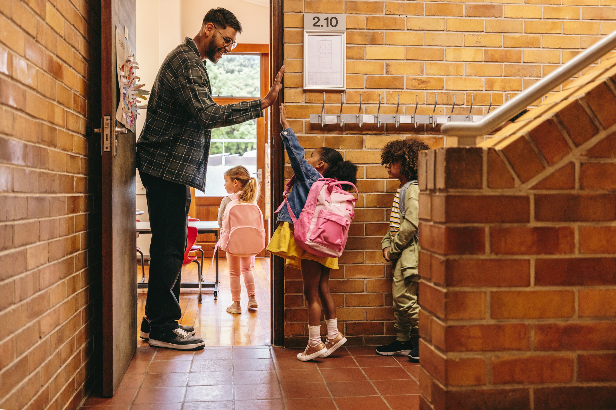 Male teacher greets young children at classroom door.