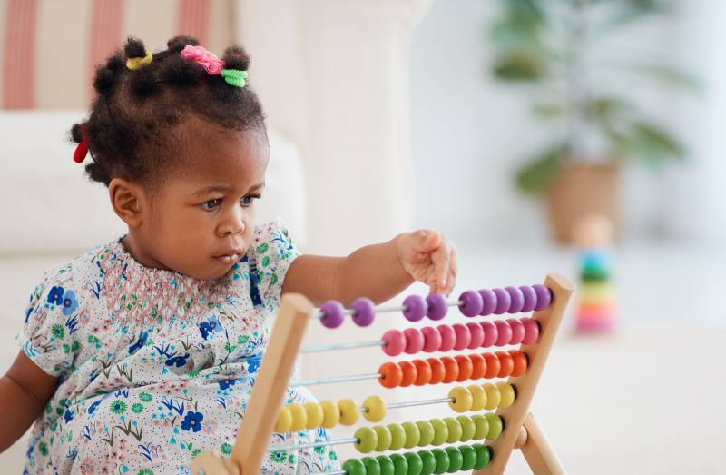 very young child sits on the floor and plays with a colorful abacus