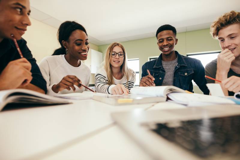 Multiracial group of teens studying around a table covered with books