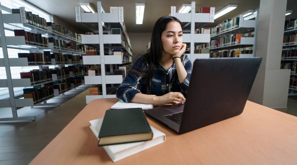 Female student using laptop at table in library