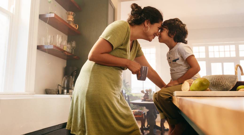 Affectionate mother touching noses with her young son in the kitchen.