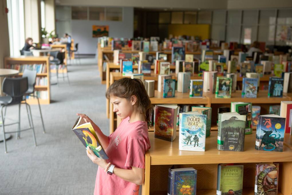 A seventh-grade student reads a book in the library stacks at Sutton Middle School.