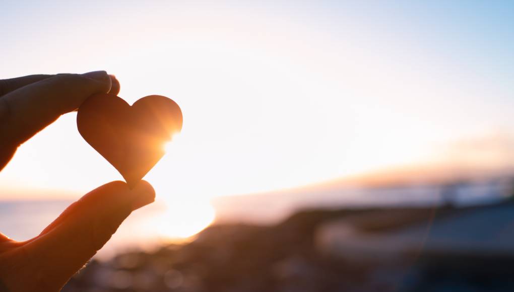 Hand holding heart in the sunset.