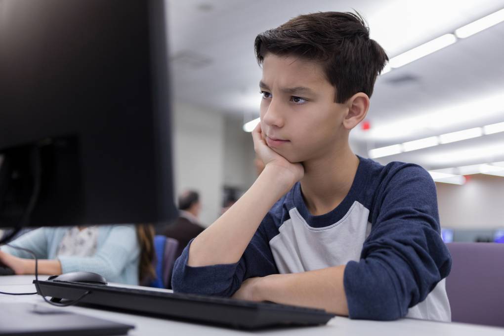 Thoughtful middle school boy looks with curiosity at a computer monitor while in his school's computer lab.