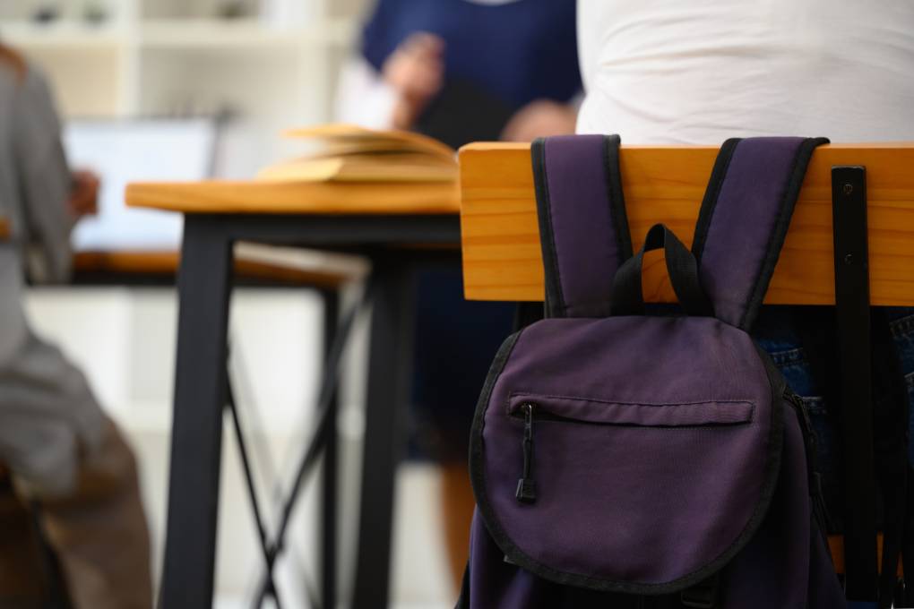 School backpack hanging on a wooden chair in classroom.