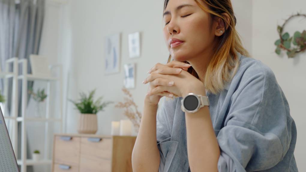 Woman with eyes closed and hands clasped in meditation or frustration.