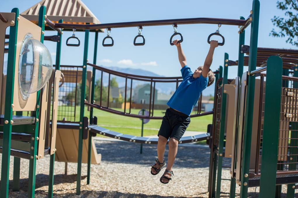 Young boy hanging on monkey bars at the park.