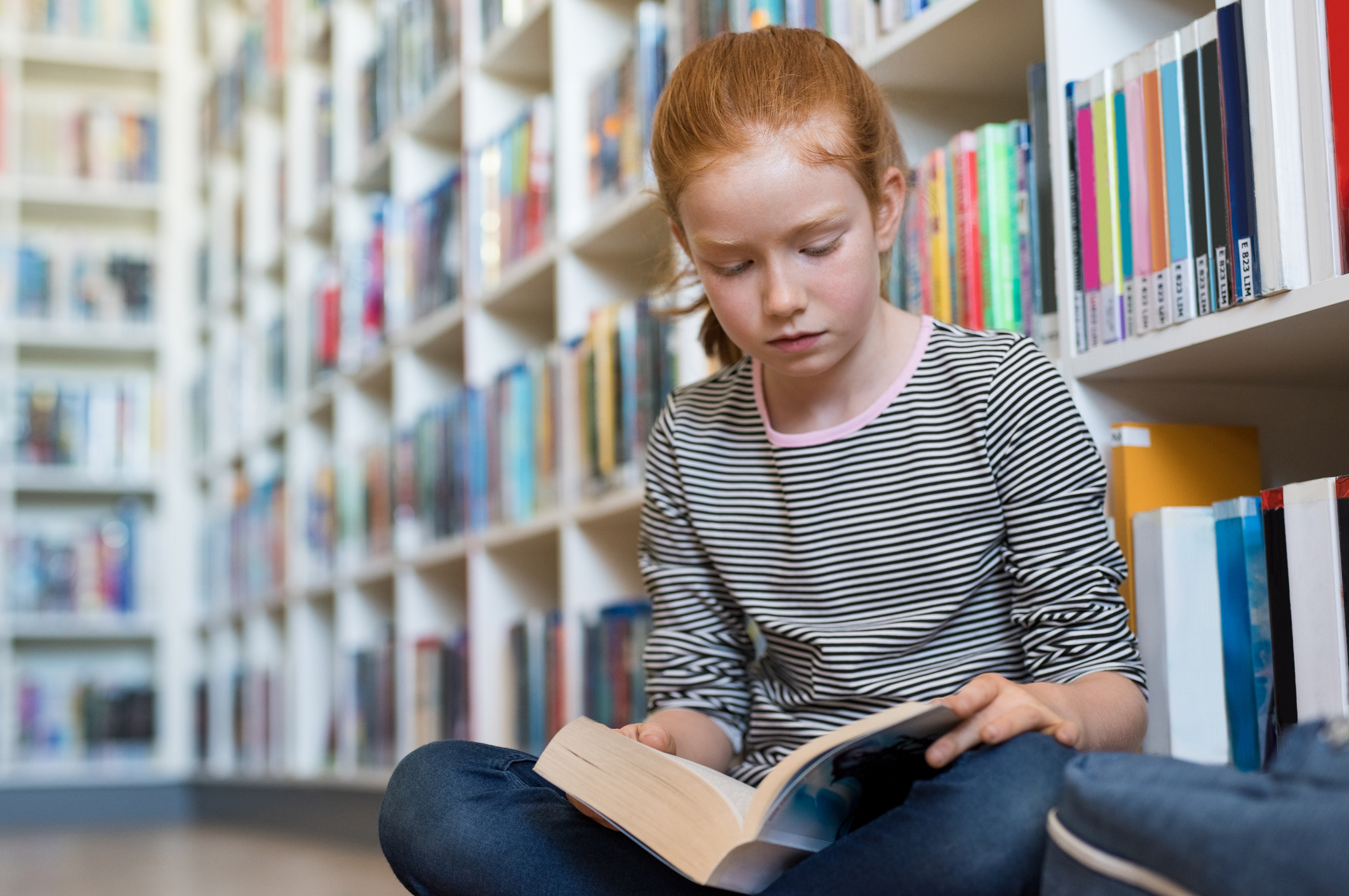 Red-haired elementary school age girl reading a book in a library