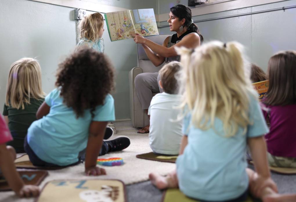 Teacher holding up book to read to children sitting on the ground.