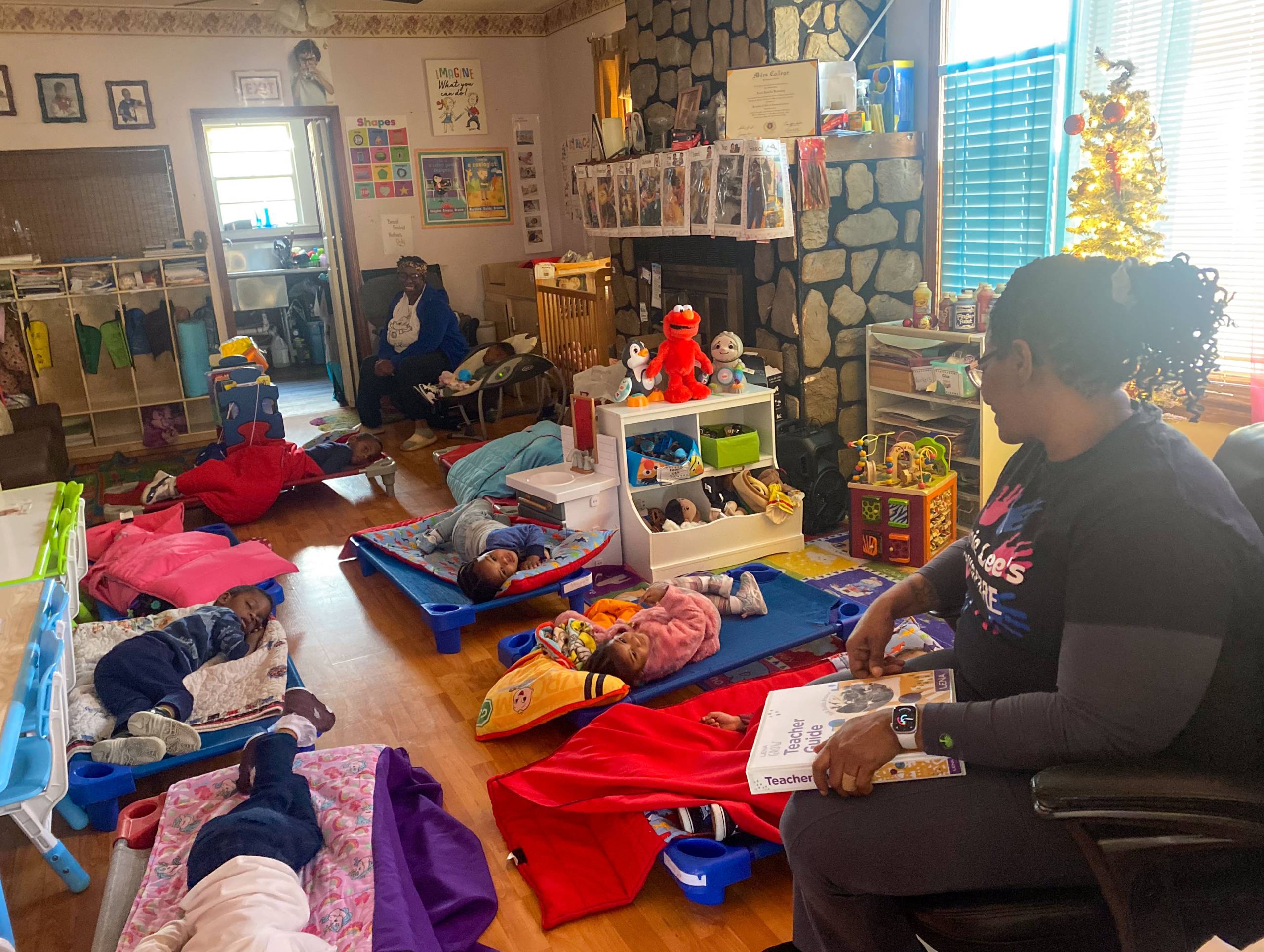 Children napping on cots in a preschool while teacher looks on