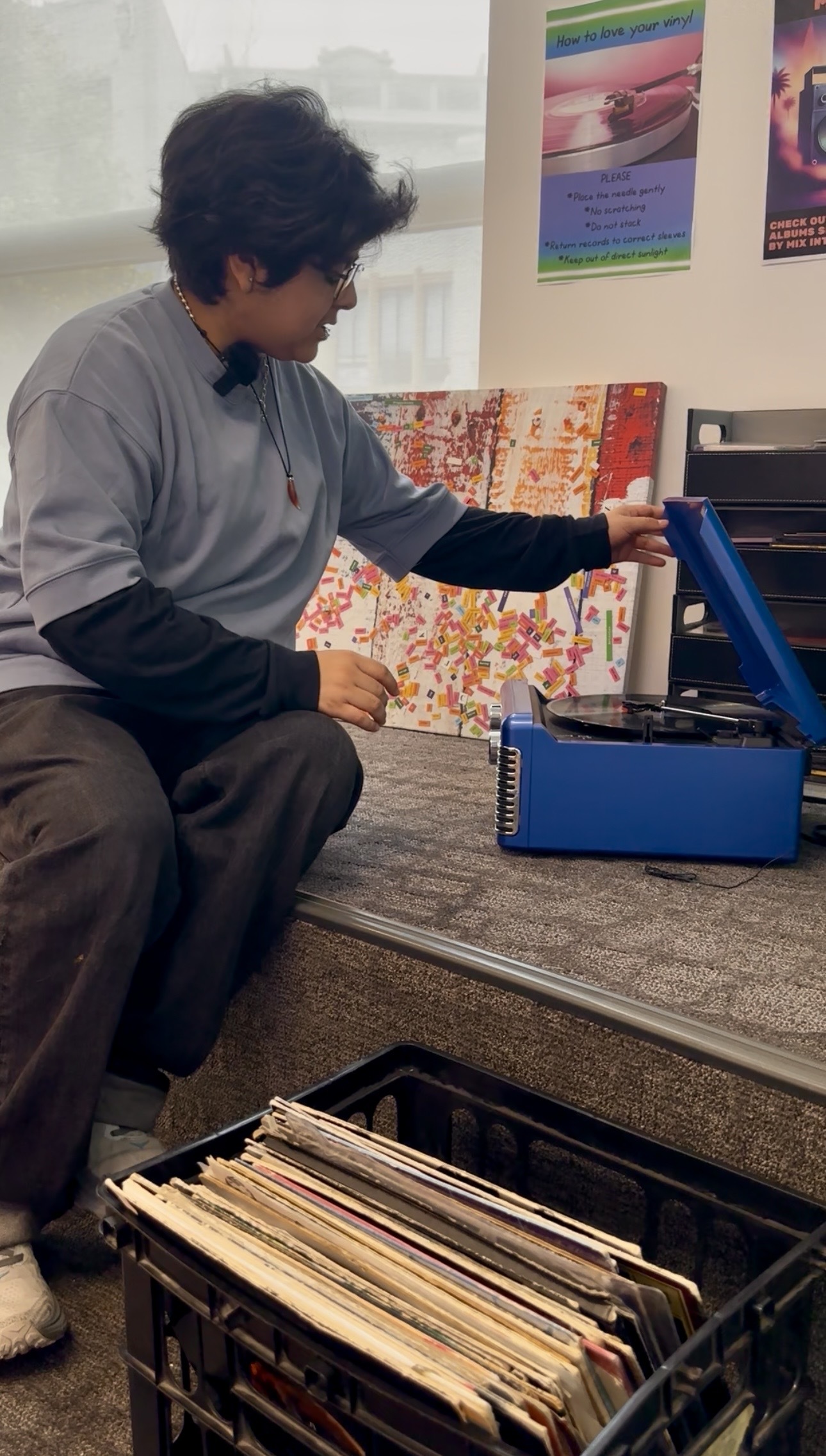 Teen opening record player with crate of records at his feet.