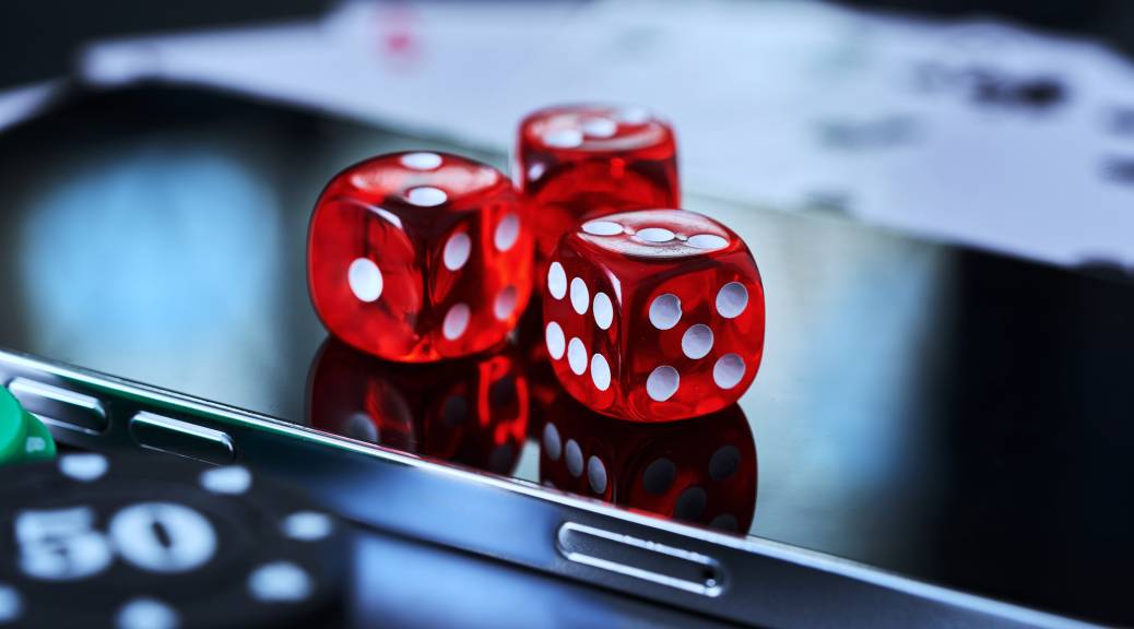 Dice resting on a smartphone alongside poker chips and playing cards