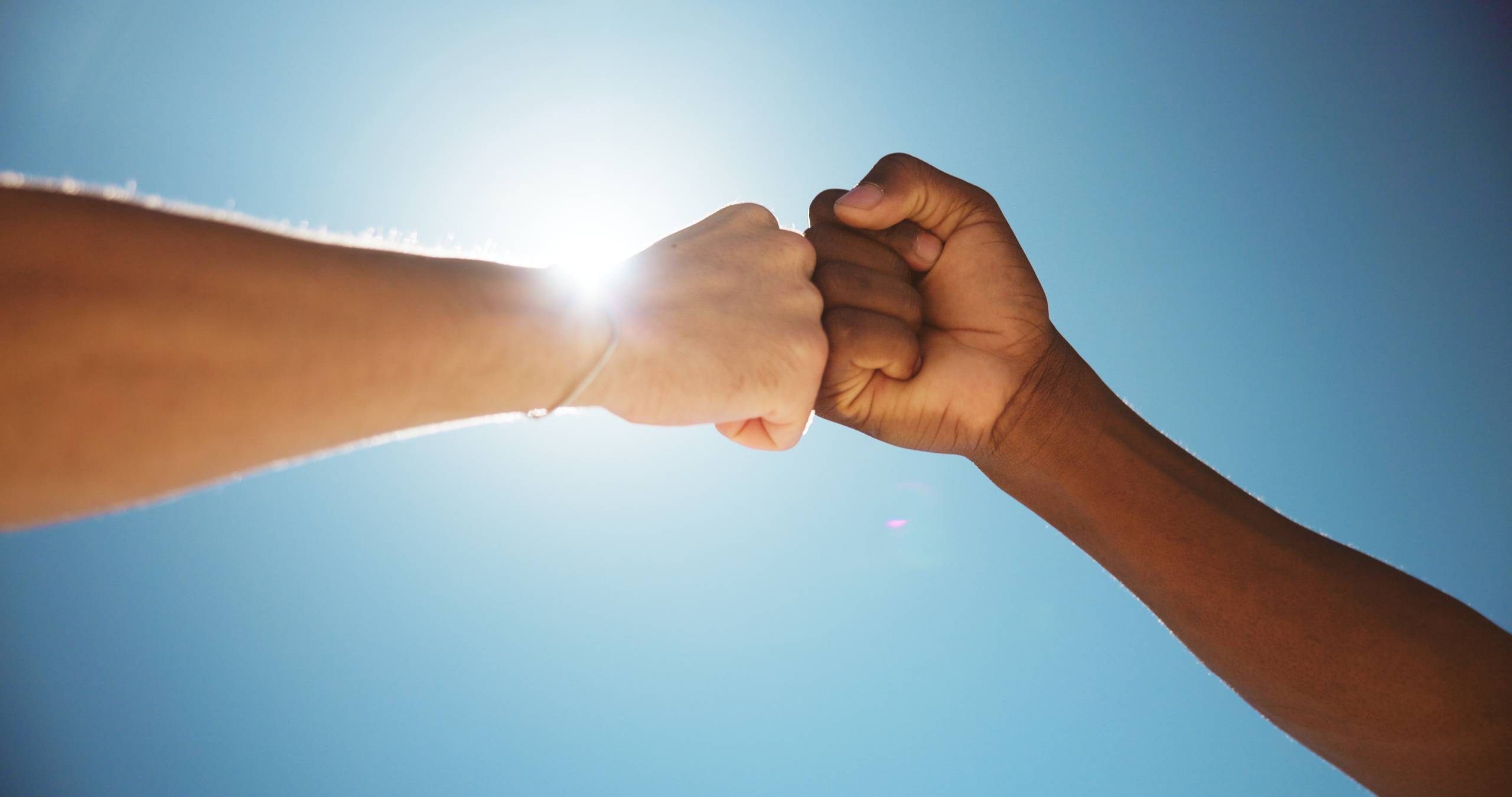 Two people fist bump with sunbeams shining in background
