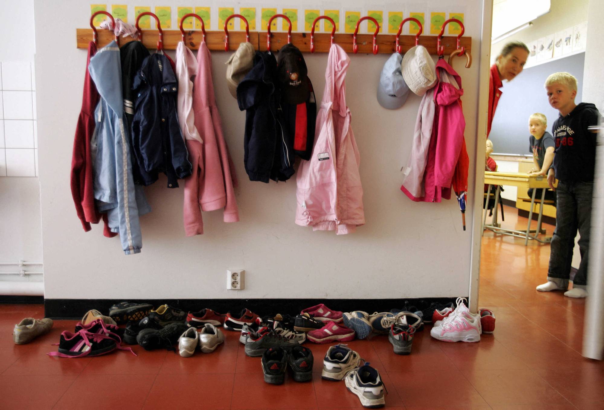 Coats hang on hooks above shoes outside of a classroom