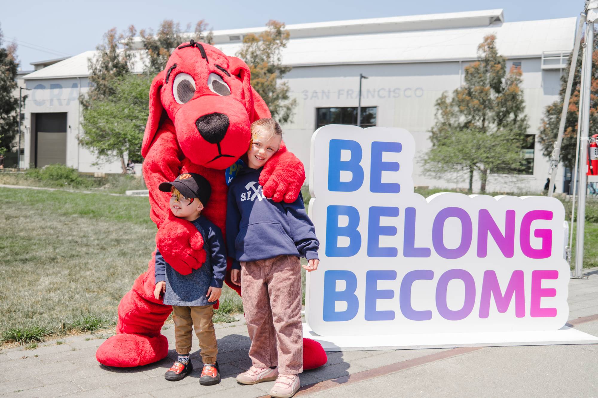 Clifford the Big Red Dog mascot hugging two kids