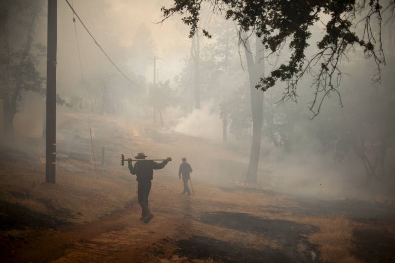 Two people walk through a smokey hillside.