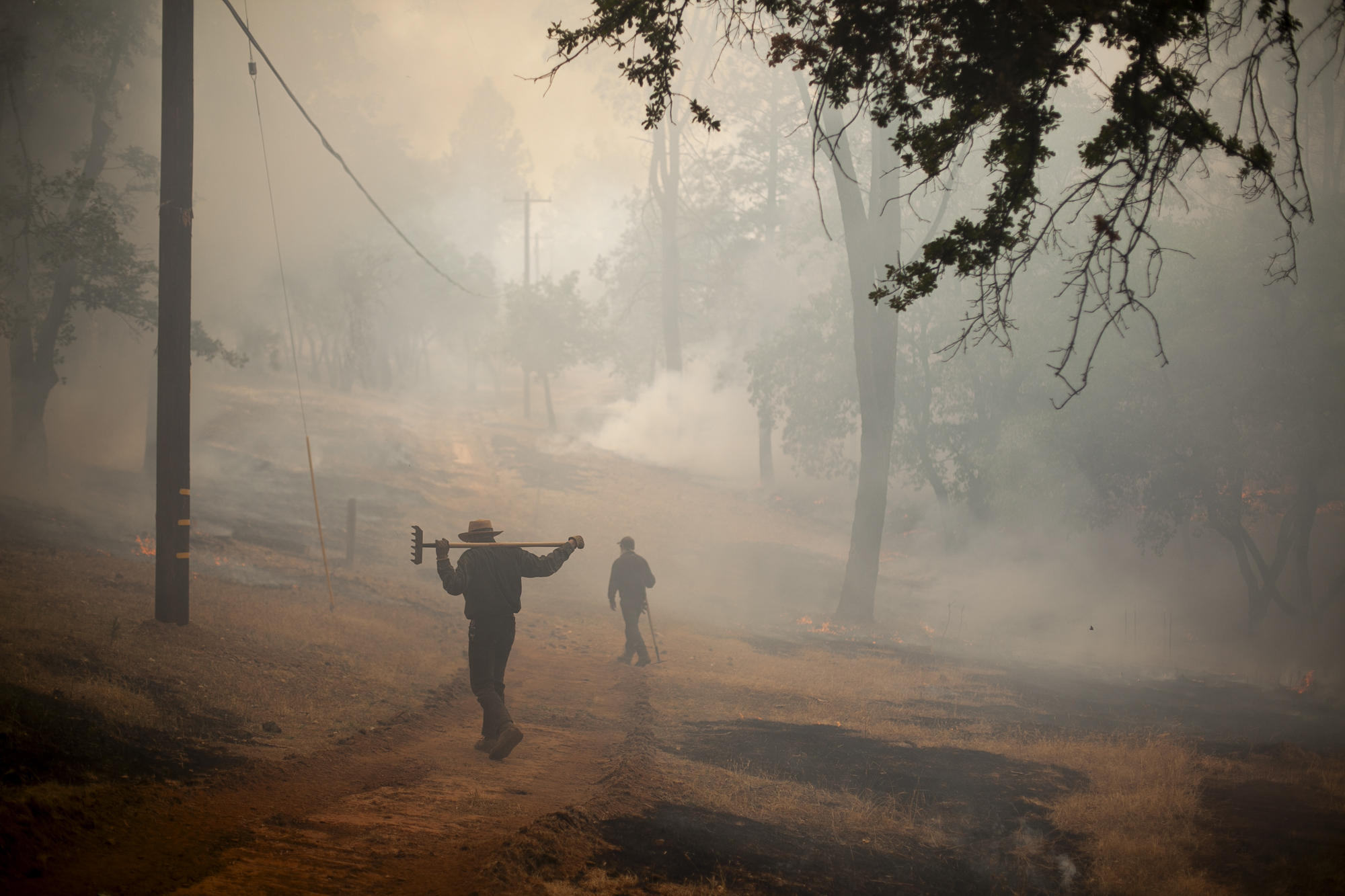 Two people walk through a smokey hillside.