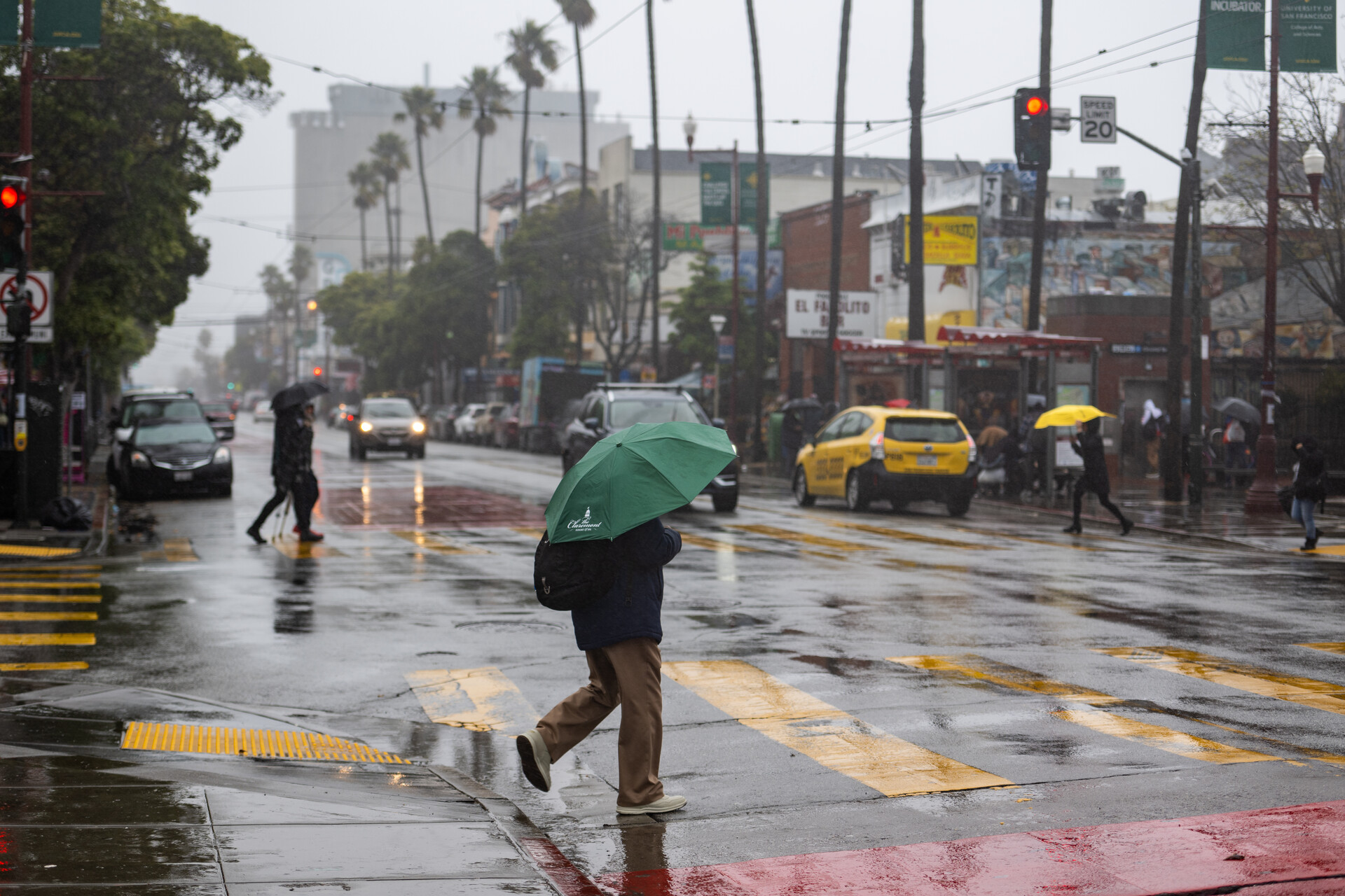 A person with a green umbrella crosses a rain-soaked street.