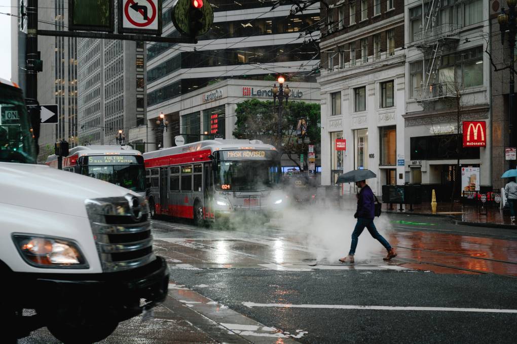 Rain falls on a red and gray bus.